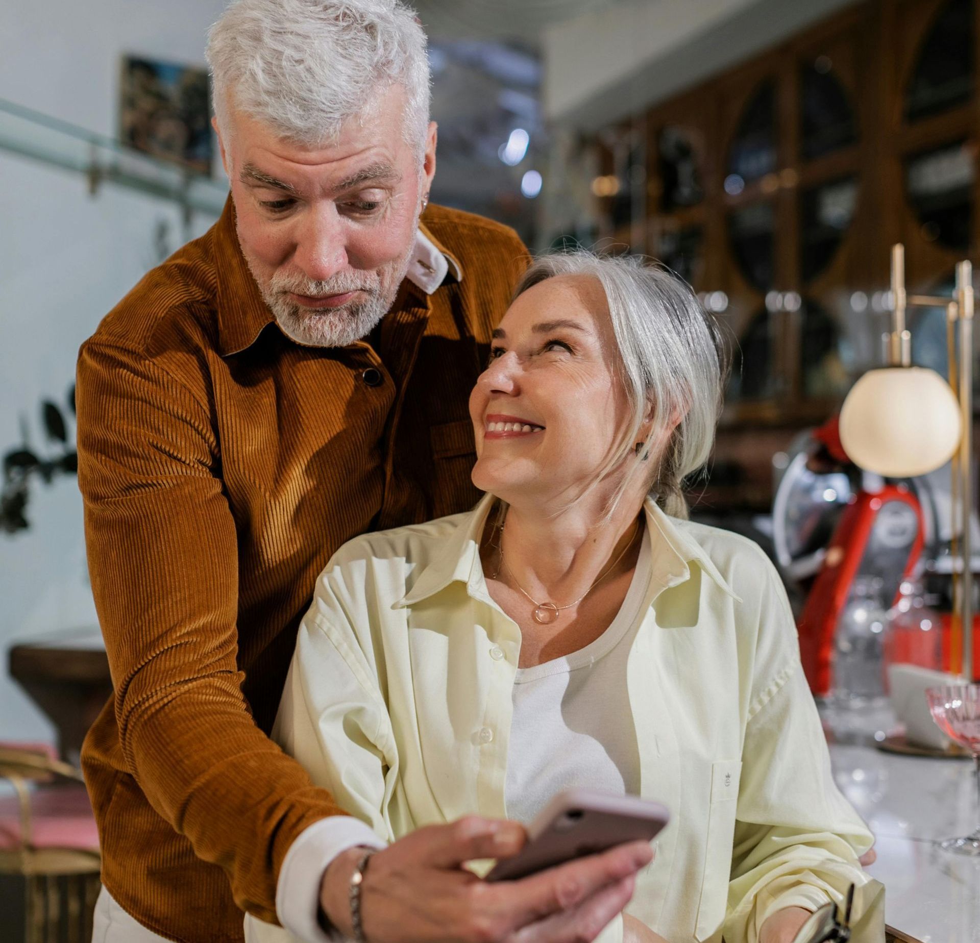 An older man and a woman are looking at a cell phone together and smiling.