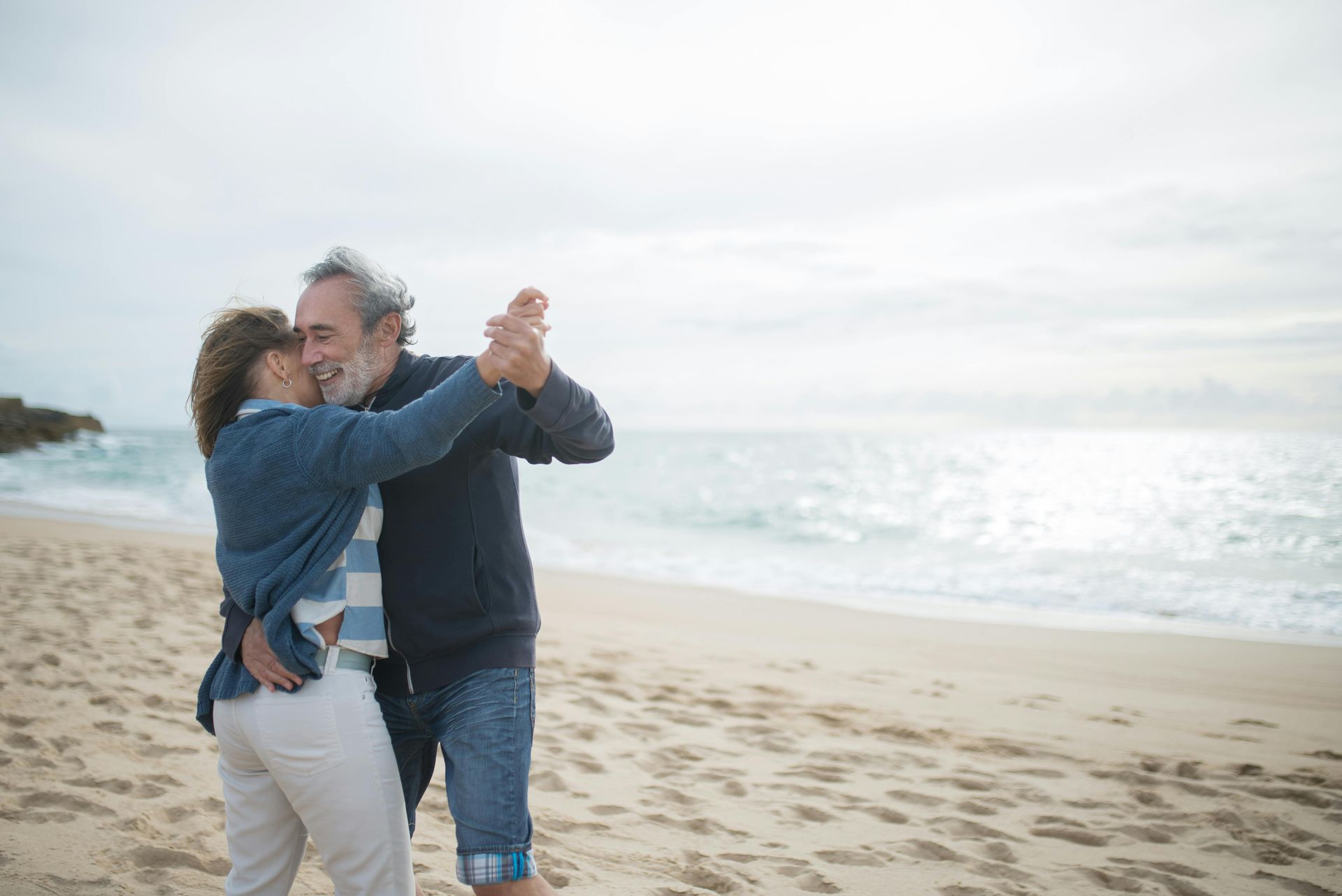 An older couple is dancing on the beach.