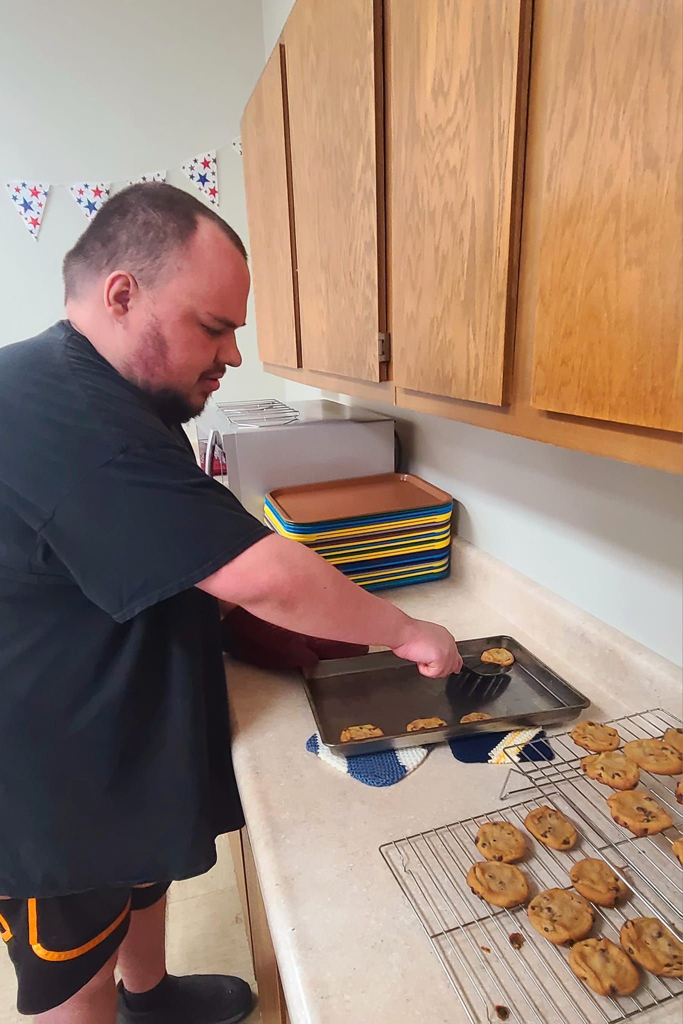 A man in a black shirt bakes cookies in a kitchen, placing them on a wire rack.