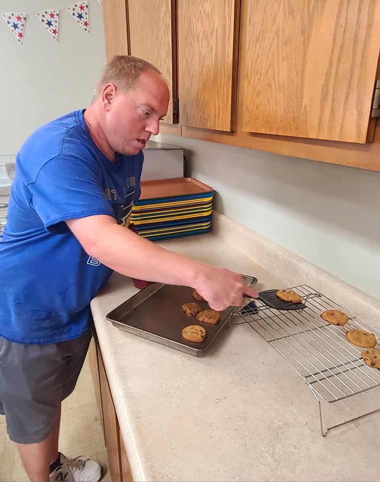 A man in a blue shirt removes cookies from a baking sheet onto a cooling rack in a kitchen.