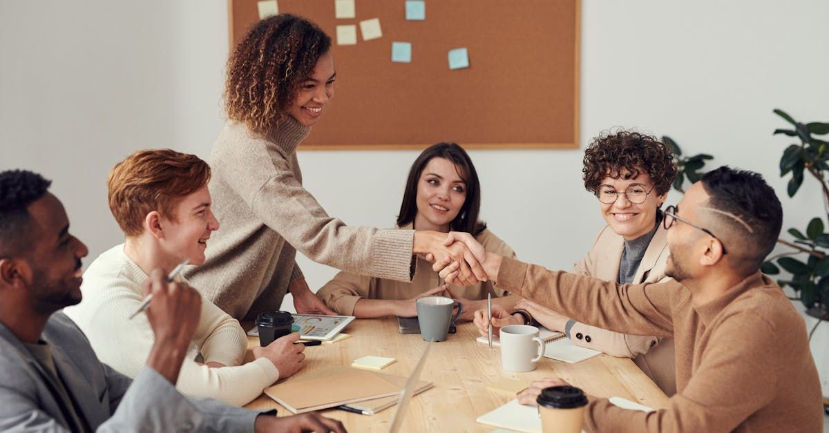 A group of people are sitting around a table shaking hands.