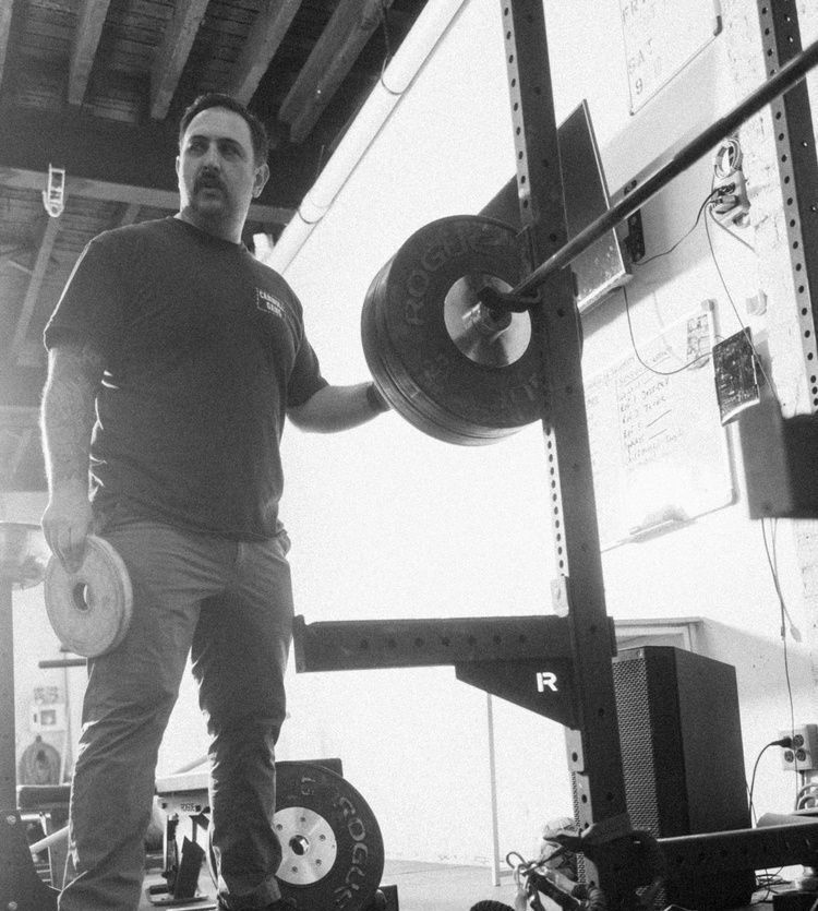 A man is standing in front of a squat rack holding a weight.