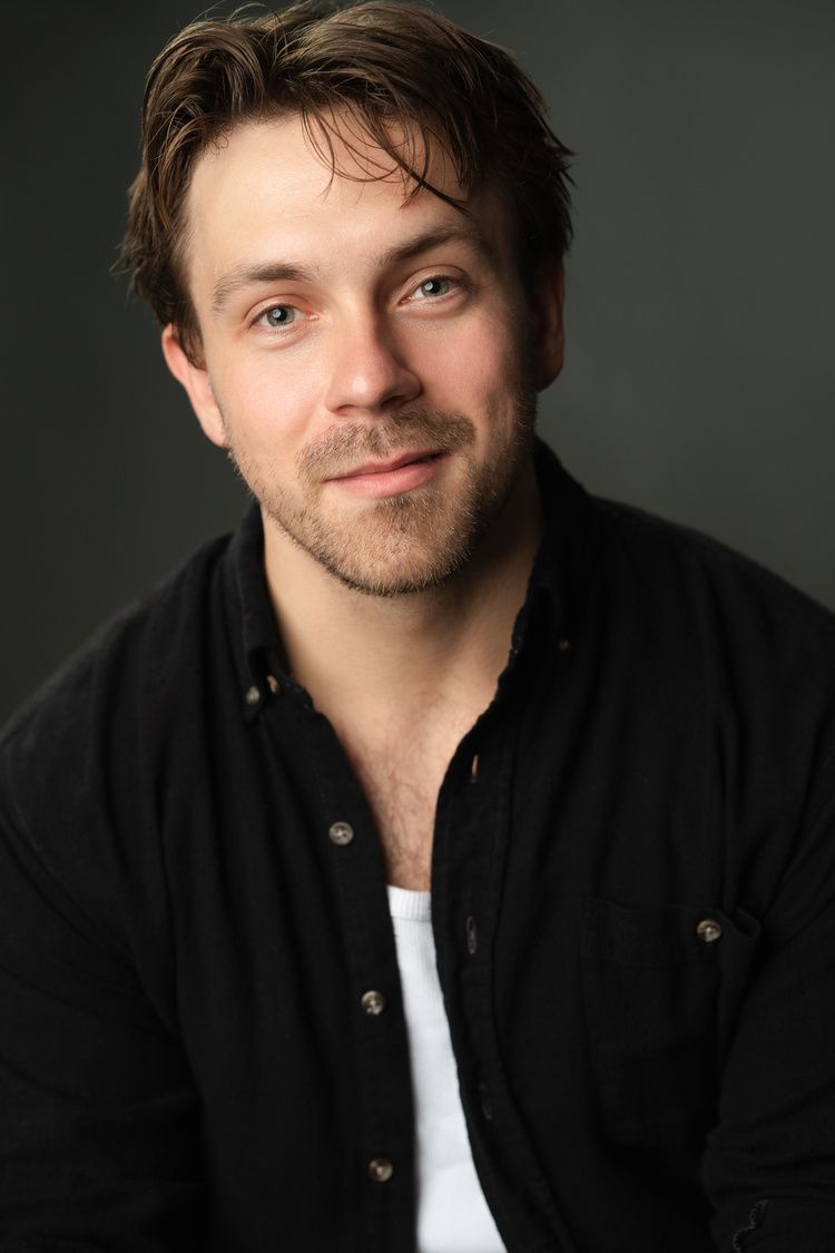 A man with a beard is wearing a black shirt and a white tank top.
