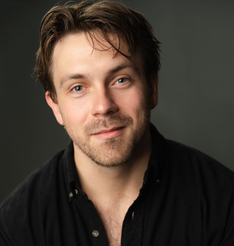 A man with a beard is wearing a black shirt and a white tank top.
