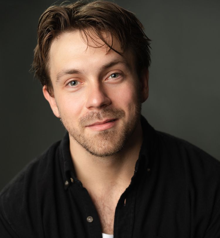 A man with a beard is wearing a black shirt and a white tank top.