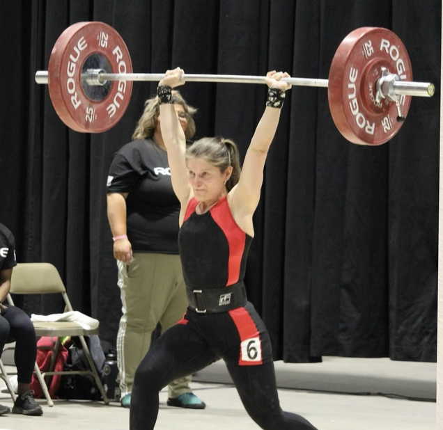 A woman lifts a barbell with the number 6 on her belt