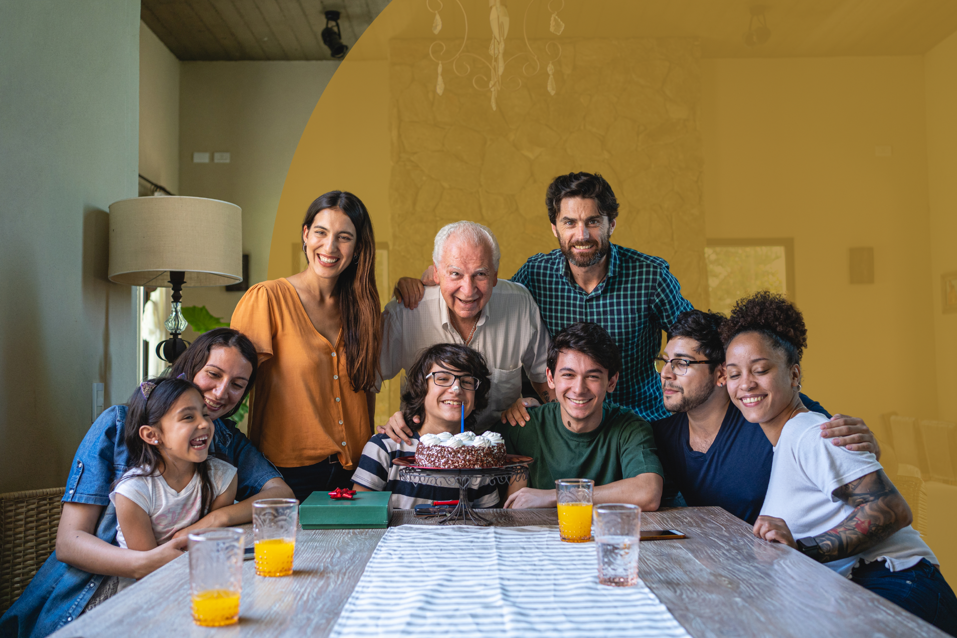 A large family is sitting around a table with a cake.