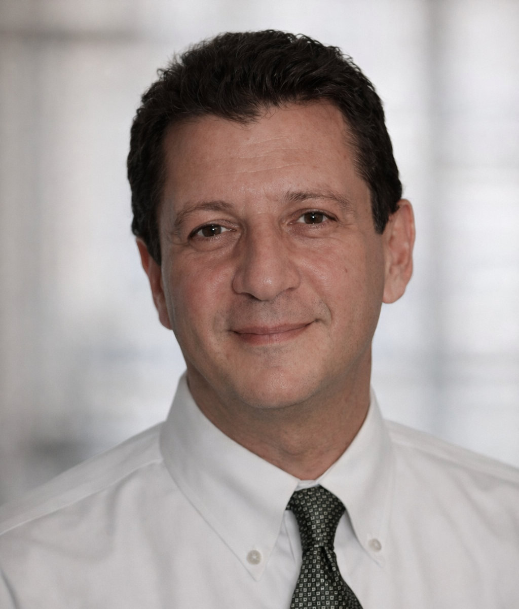 Man in white shirt and patterned tie smiles, head and shoulders shot, blurred background.