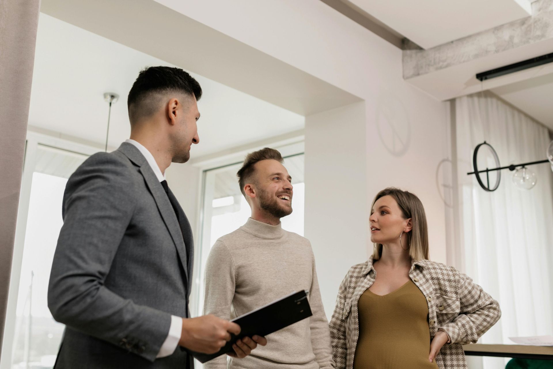 Real estate agent showing a home to a couple. Agent in suit, holding documents. Couple smiling.