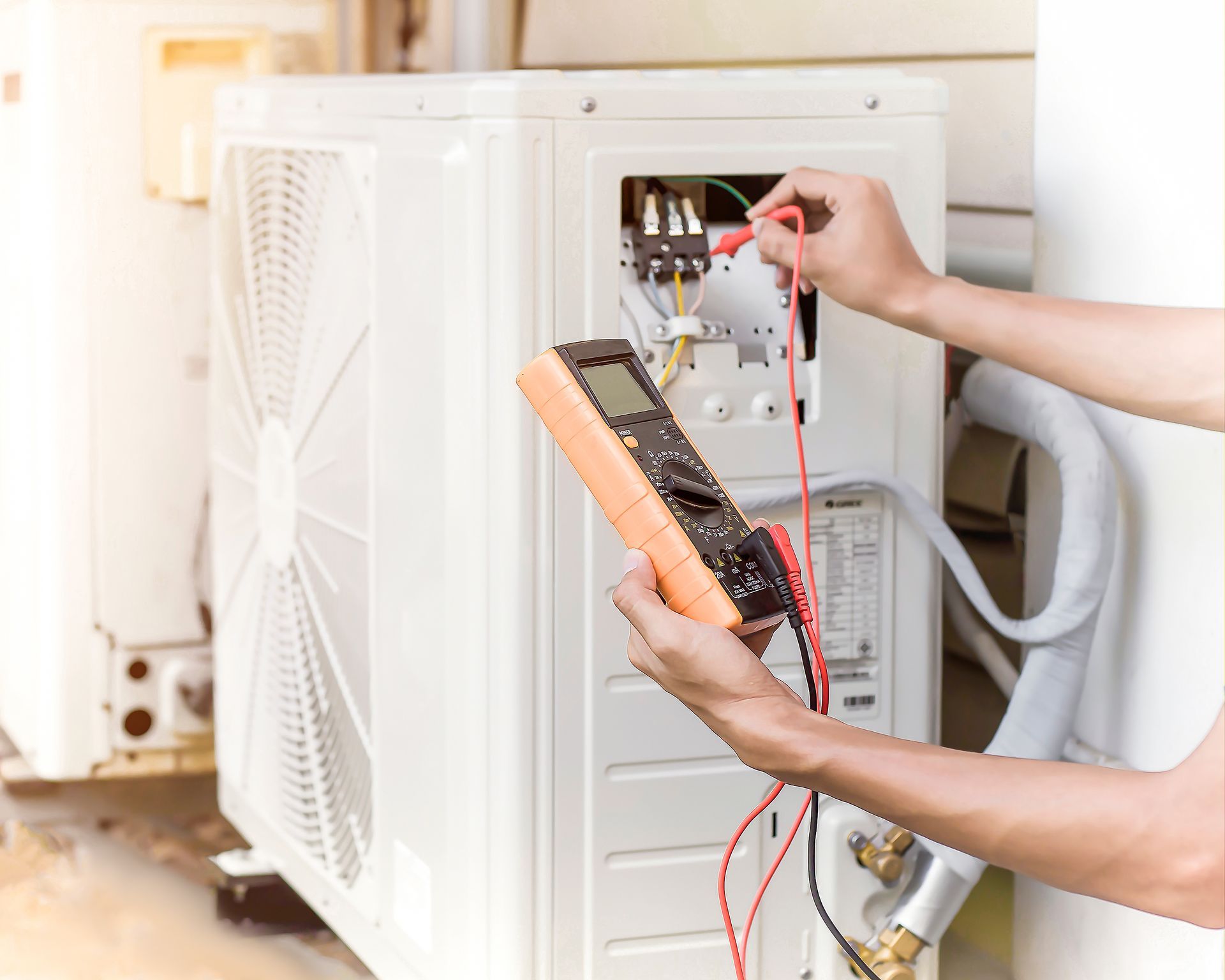 Technician testing an outdoor air conditioner unit with a multimeter and wires exposed