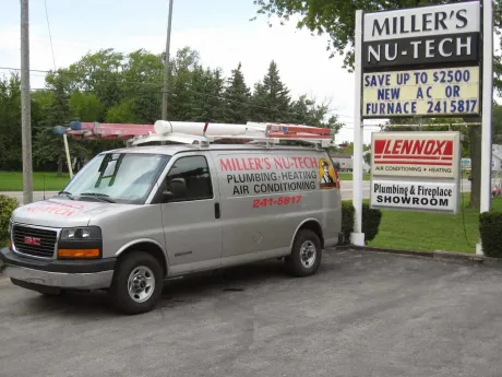 A silver work van parked beside a business sign for Miller's Nu-Tech, advertising HVAC and plumbing services.