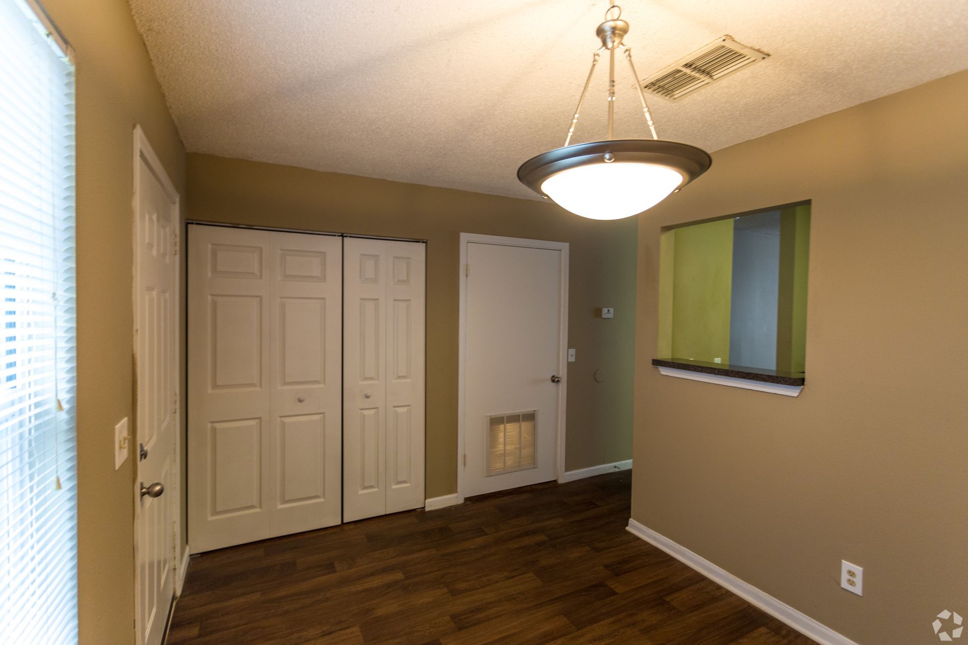 An empty room with dark wood floors, tan walls, a light fixture, a closed closet, and a door with a pet flap.