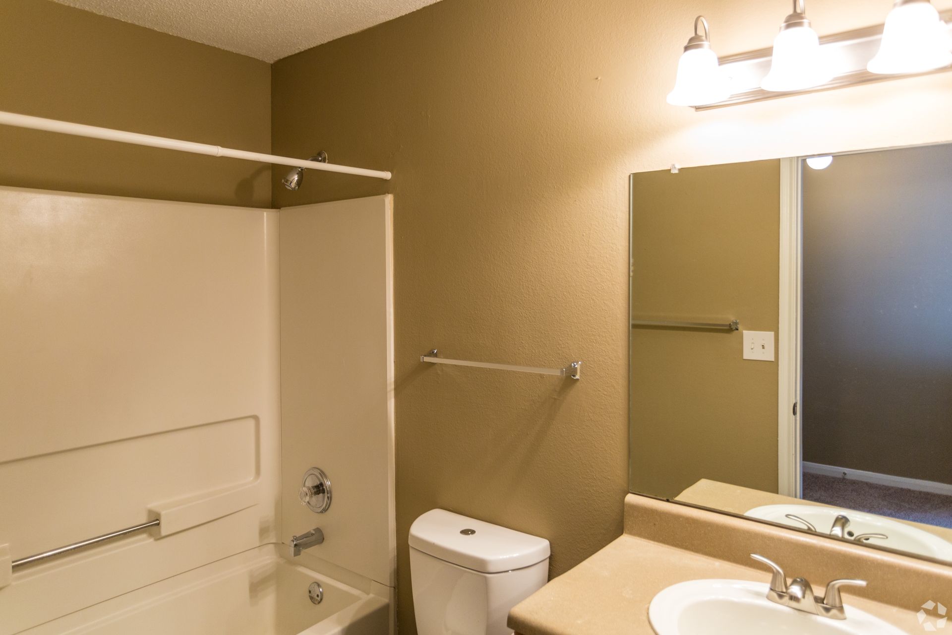 A beige-toned bathroom featuring a bathtub and shower combination, a white toilet, and a vanity with a mirror.