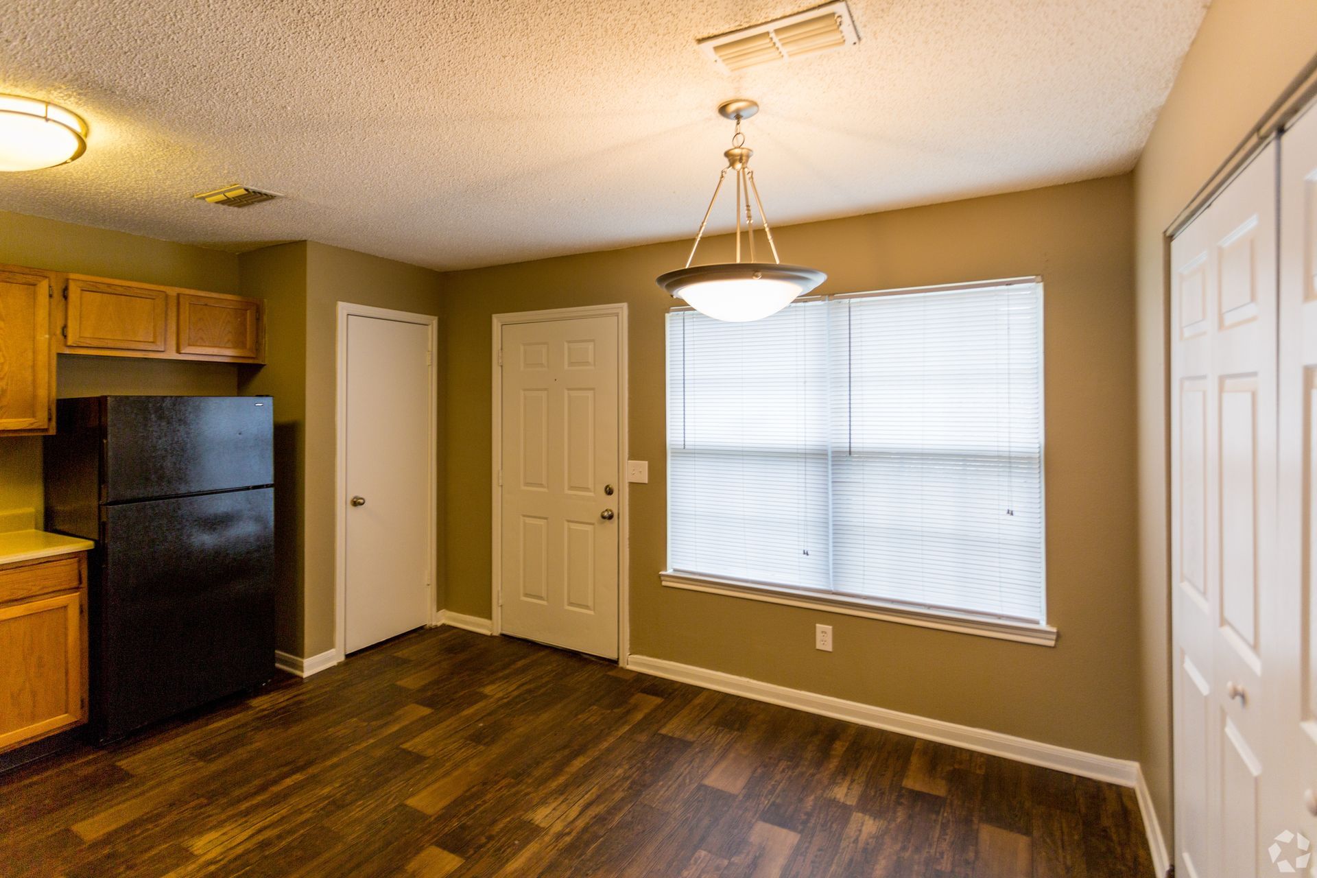 Kitchen featuring a black refrigerator, wooden cabinets, a dining light fixture, a window with blinds, and brown flooring.