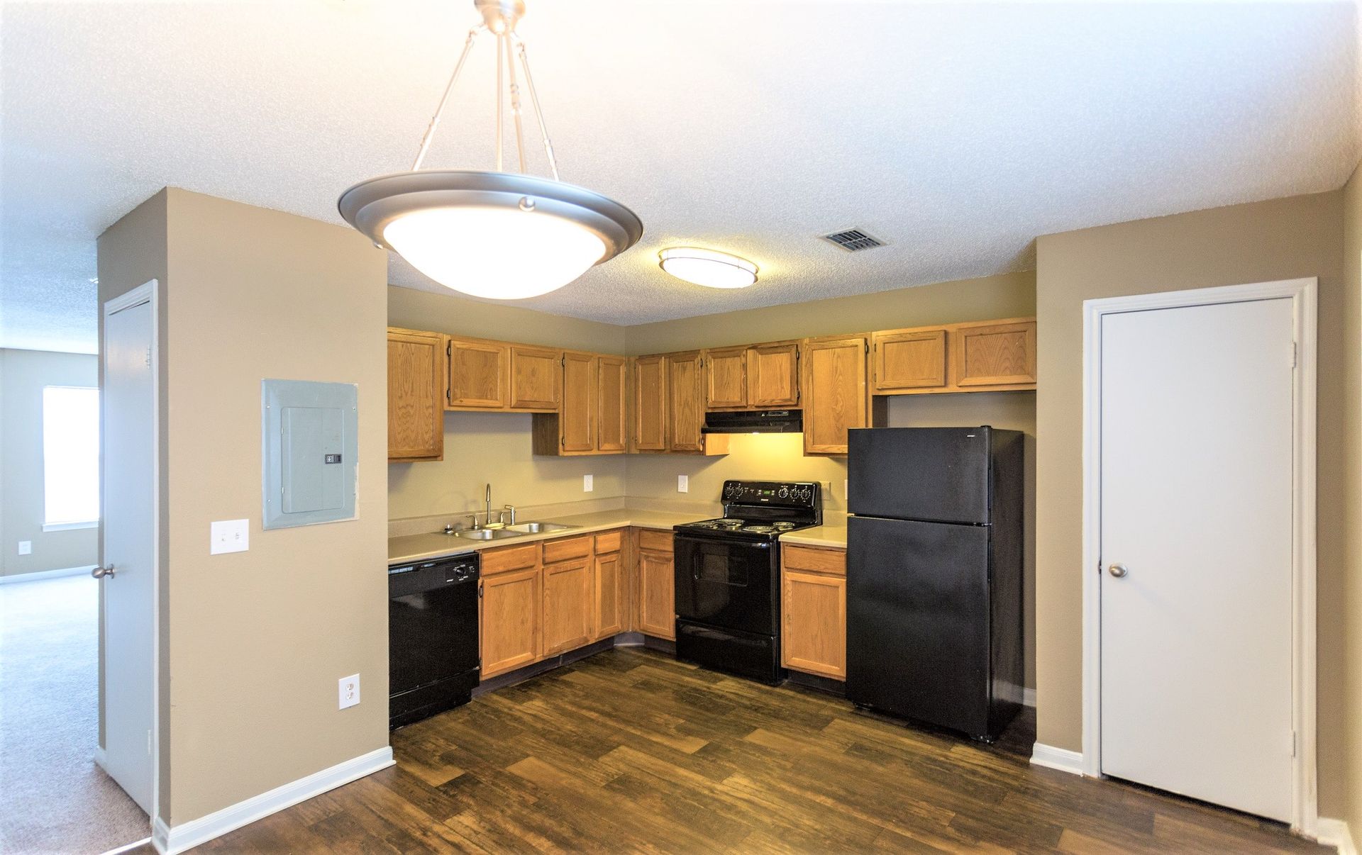 A kitchen with wooden cabinets, black appliances, dark wood-look flooring, and a round pendant light above.