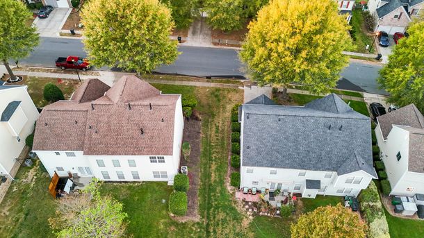 Aerial view of two-story houses with brown and grey roofs, separated by a grassy strip, on a suburban street.
