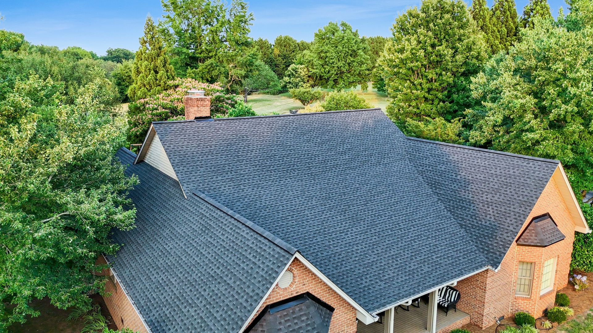 Brick house with dark blue wavy roof surrounded by green trees.