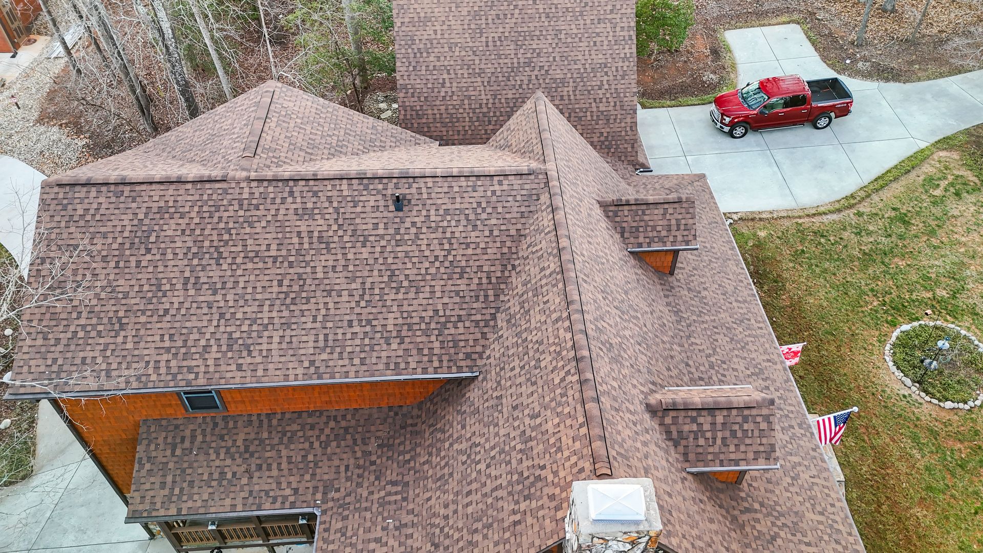 Brown shingle roof of a house, red pickup truck in driveway, and grassy yard.