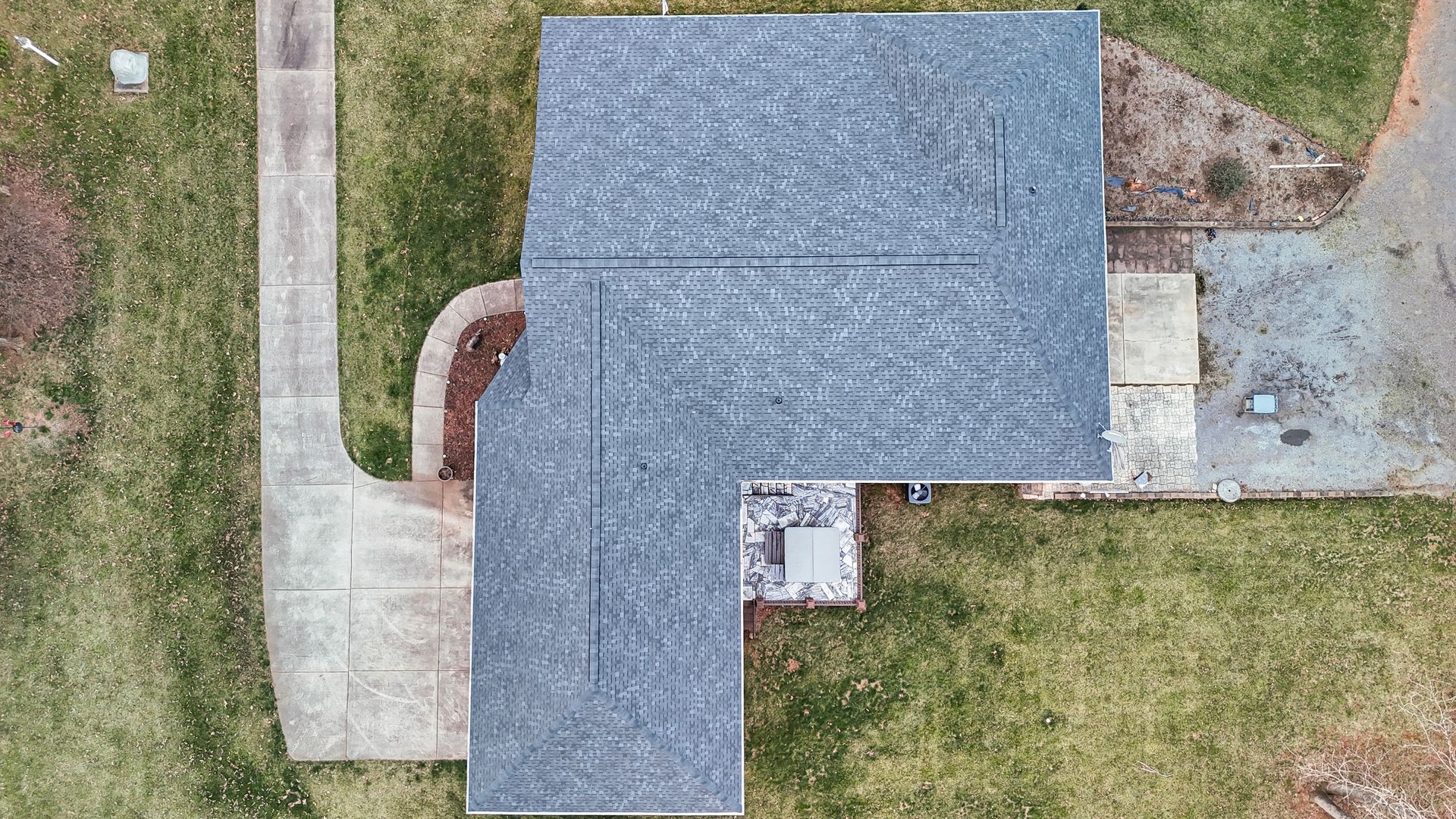 Overhead view of a house with a gray shingle roof, surrounded by lawn and a concrete walkway.