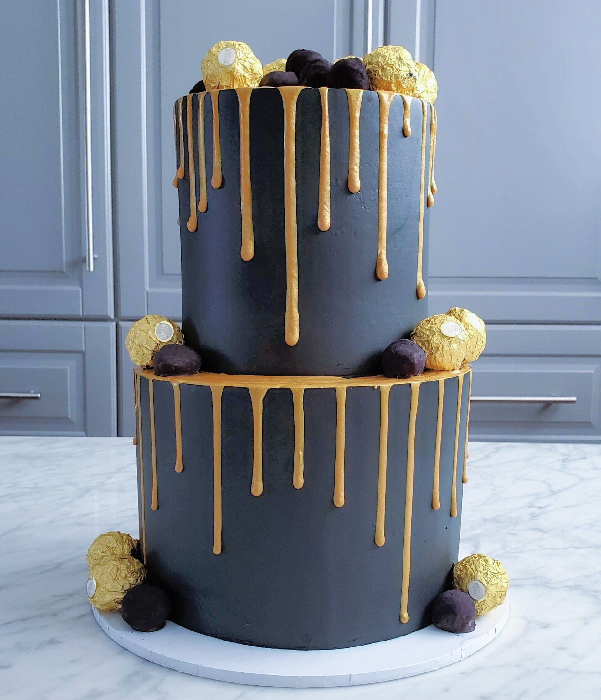 two tier black and gold cake with chocolate balls