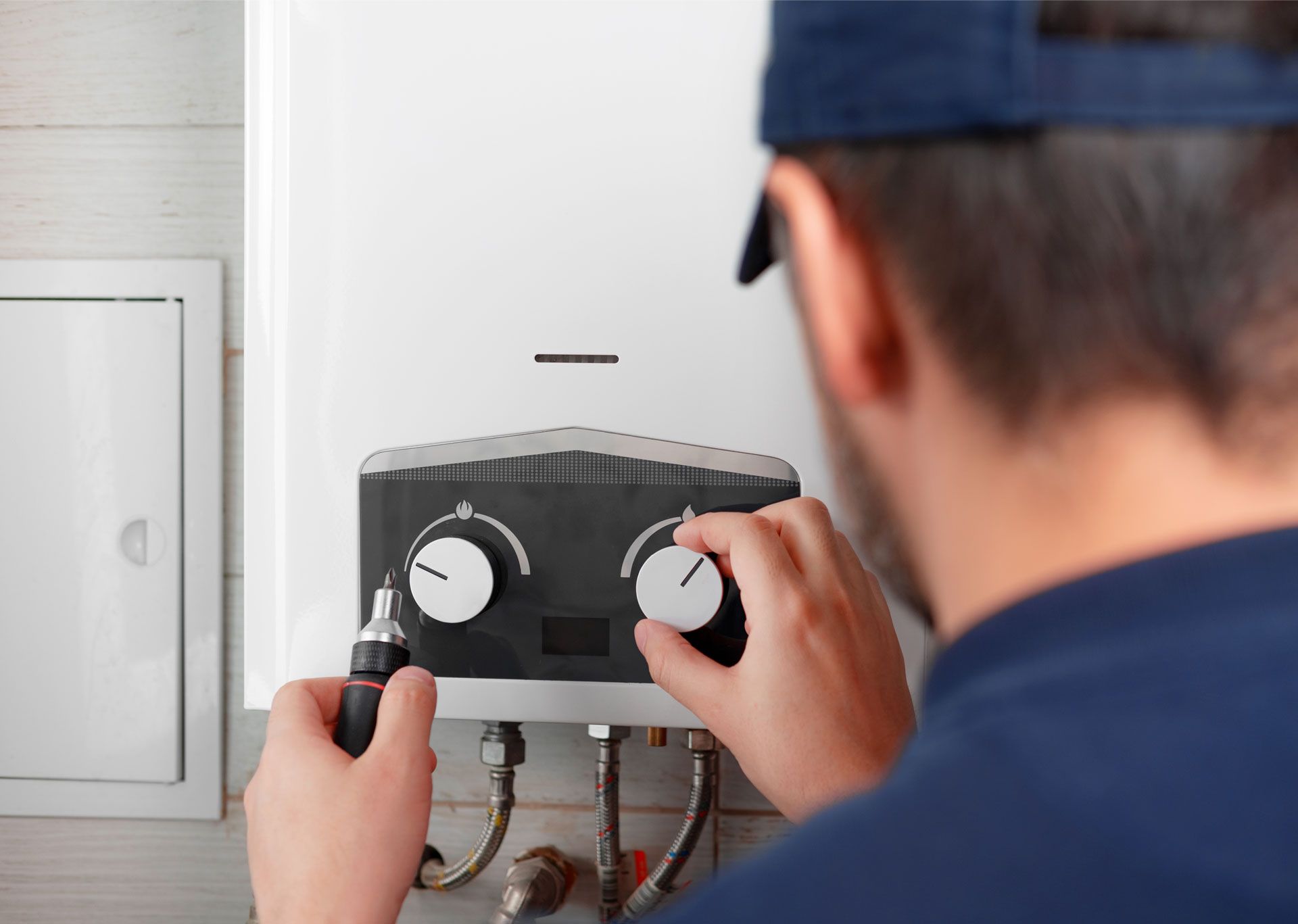 Technician adjusting a wall-mounted boiler control panel with tools in a utility room