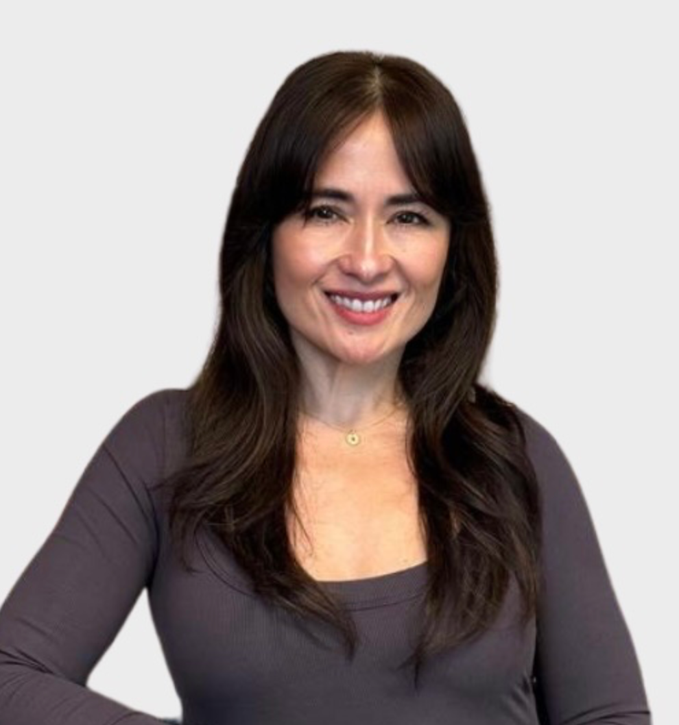 Woman smiling, dark hair, wearing a gray shirt, against a light gray background.
