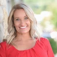 Woman in red top smiles at the camera, outdoors with blurred background.