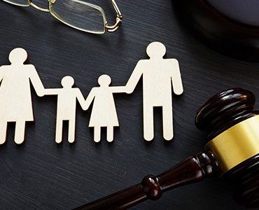 Wooden family figures, gavel, and eyeglasses on a black background, representing family law.