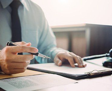 Person in light blue shirt and tie holding a pen, reviewing documents on a clipboard.