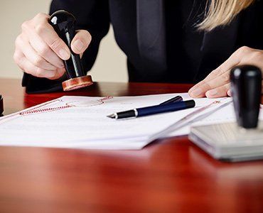 Person stamping a document with a seal on a wooden desk. A pen lies beside the paperwork.