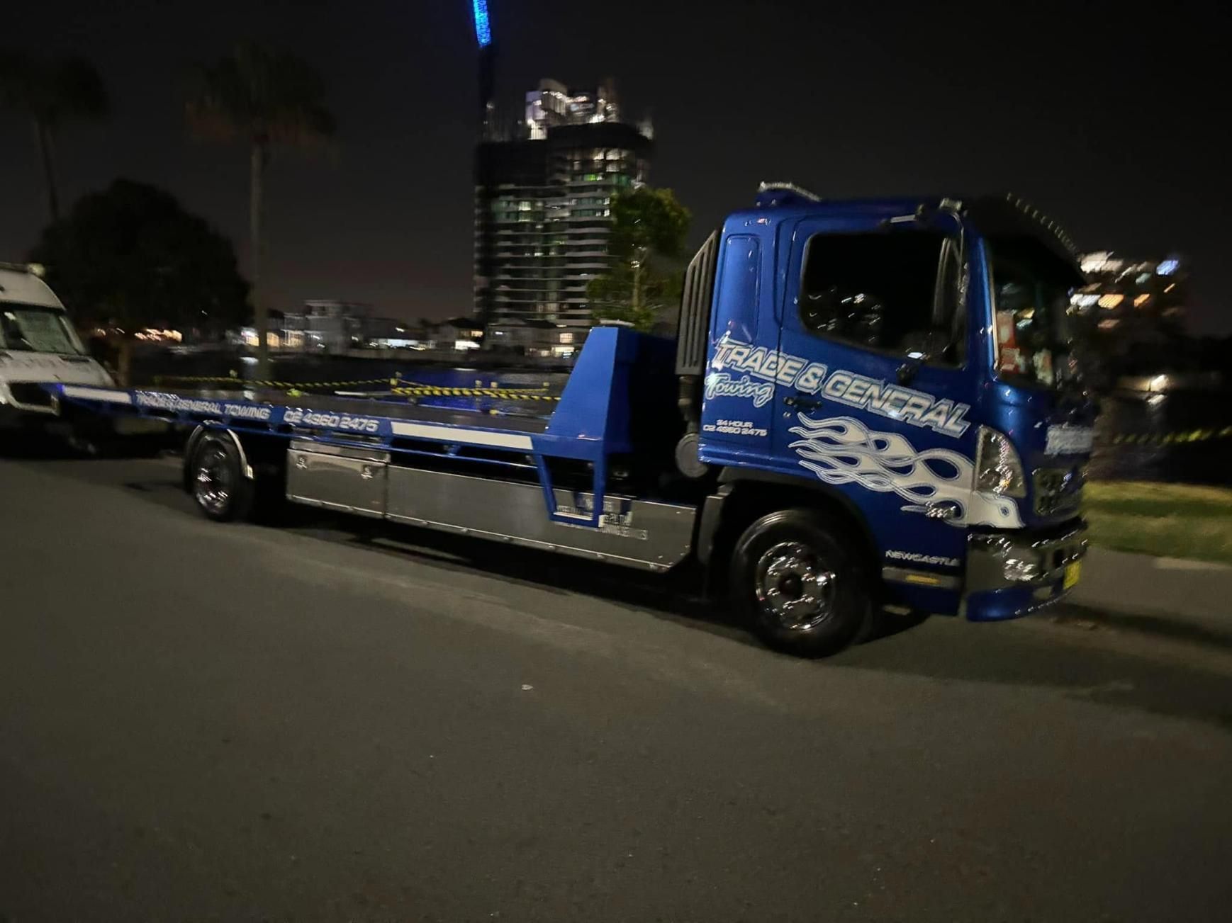 A Blue Tow Truck is Parked on the Side of the Road at Night — Trade & General Towing in Rutherford, NSW