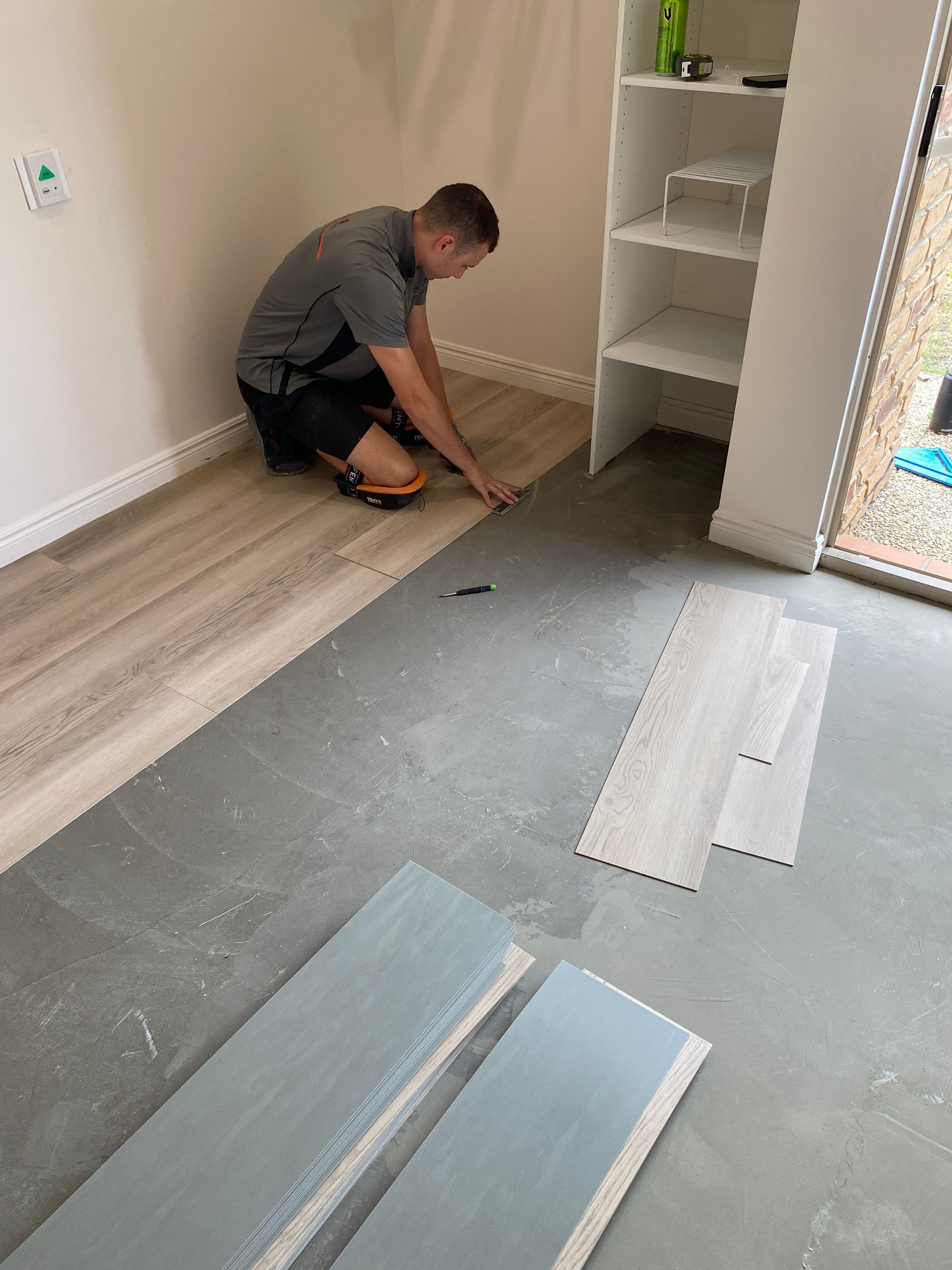 Worker installing flooring in a room with gray underlayment and white baseboards