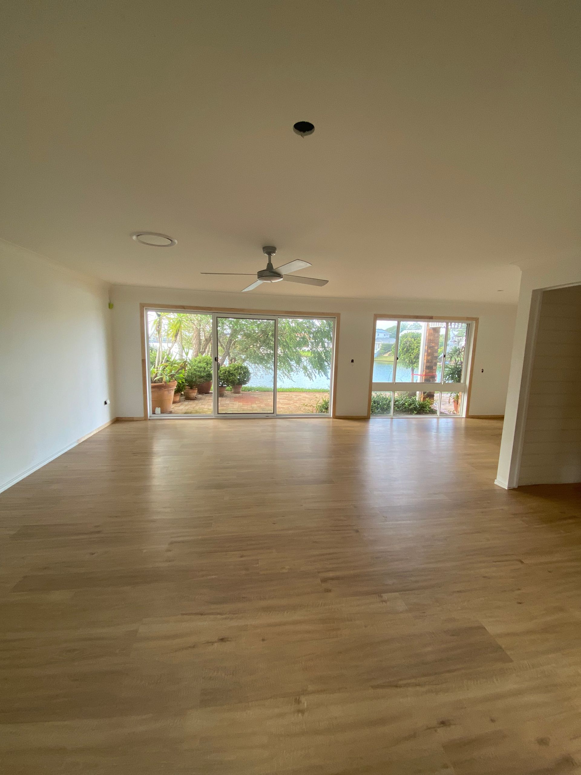 Empty modern living room with wood floors, ceiling fan, and sliding glass doors to a patio and garden.