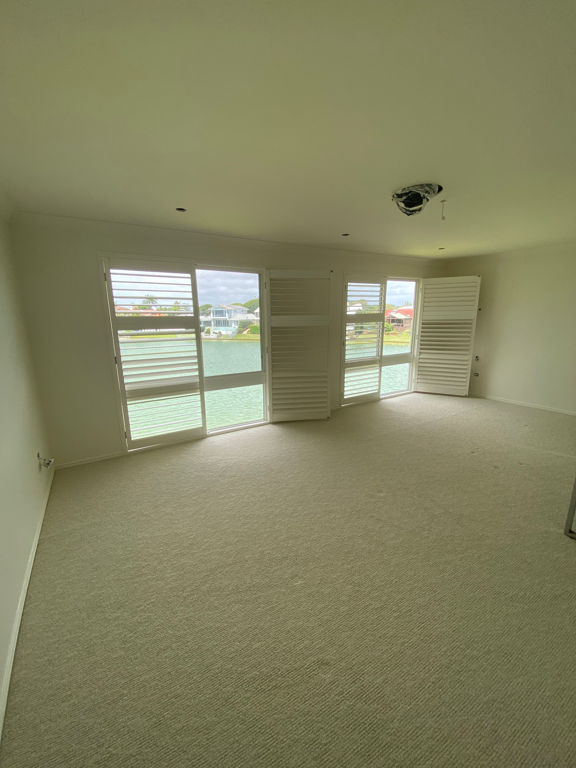 Empty carpeted living room with large windows, white walls, and ceiling light fixture