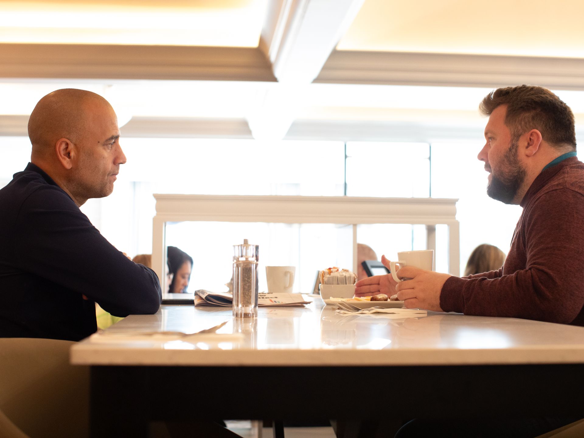 Two men are sitting at a table in a restaurant talking to each other.