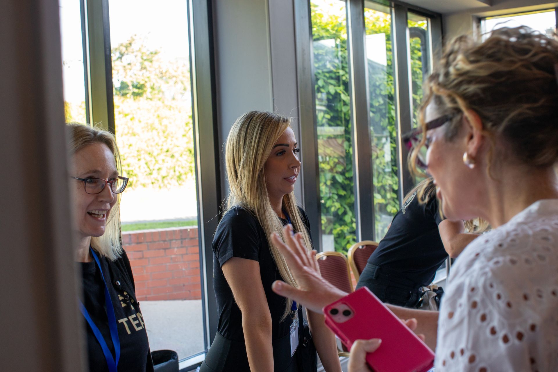 A group of women are standing in front of a window talking to each other.