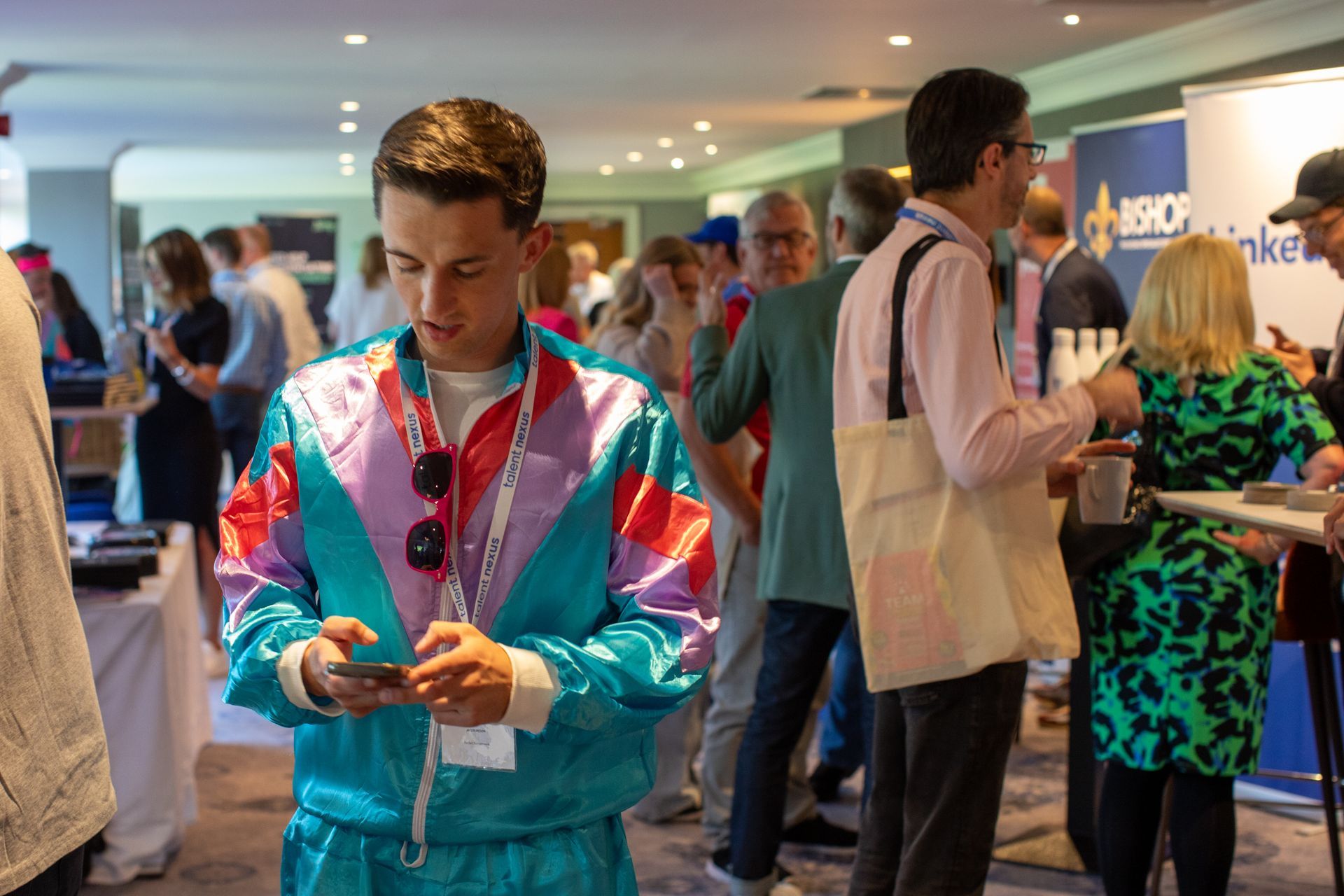 A man in a colorful jacket is looking at his phone in a crowded room.