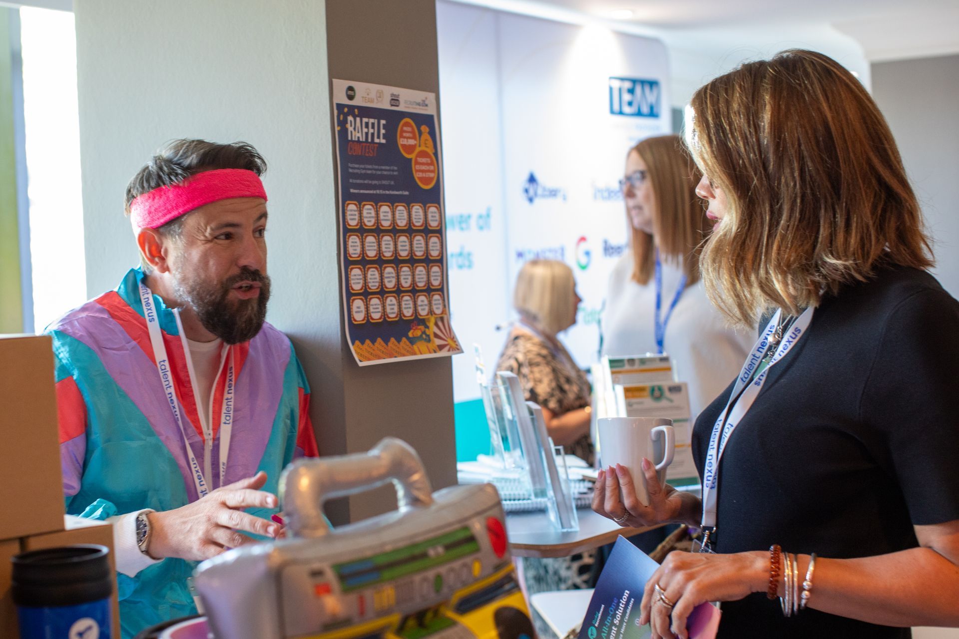 A man wearing a pink headband is talking to a woman at a table.