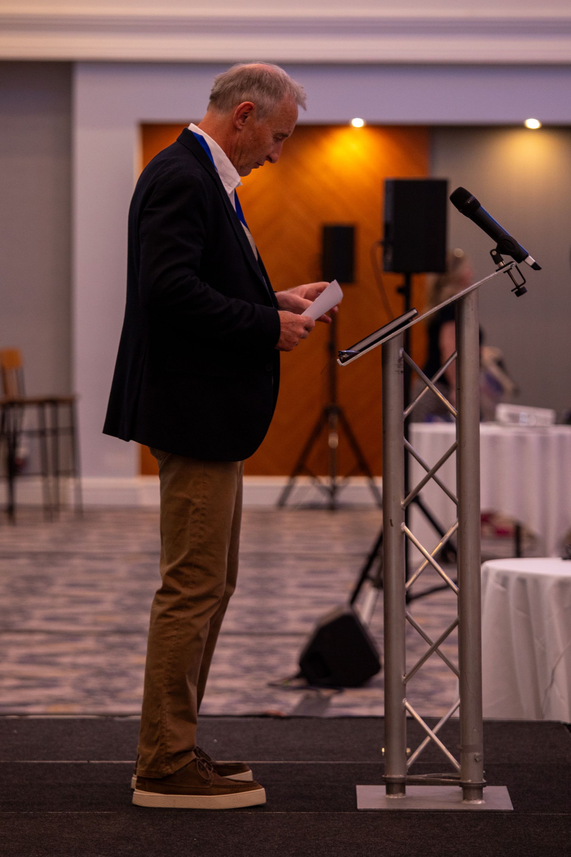 A man in a suit is standing at a podium holding a piece of paper.