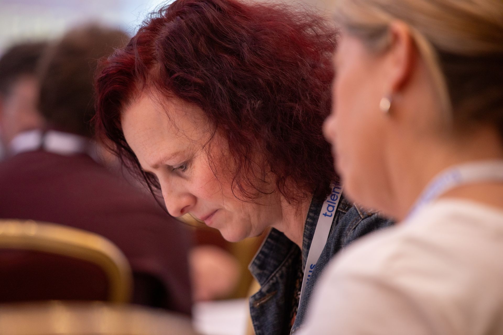 A woman with red hair is sitting at a table with another woman.