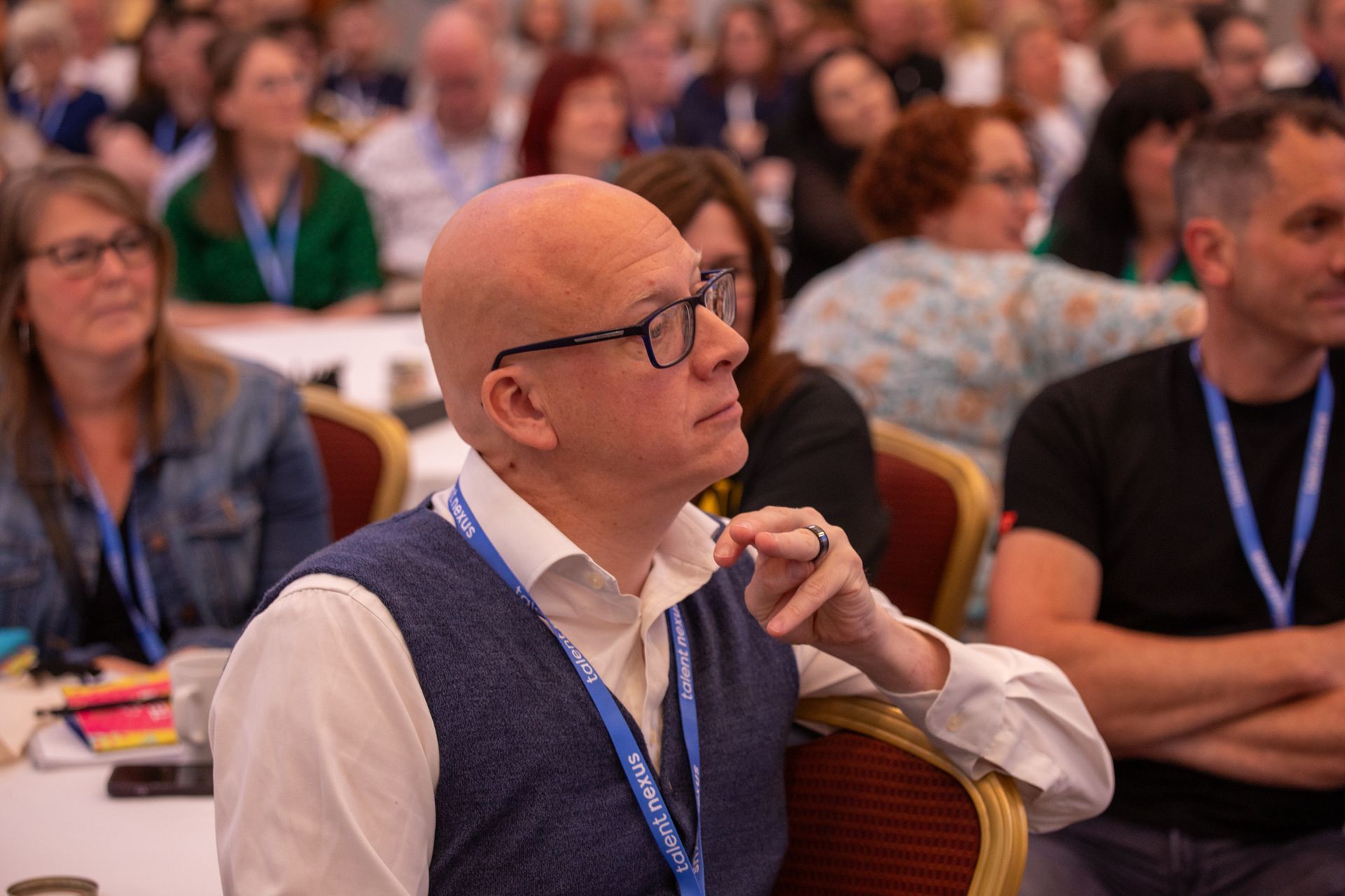 A man wearing glasses is sitting in a crowd of people at a conference.