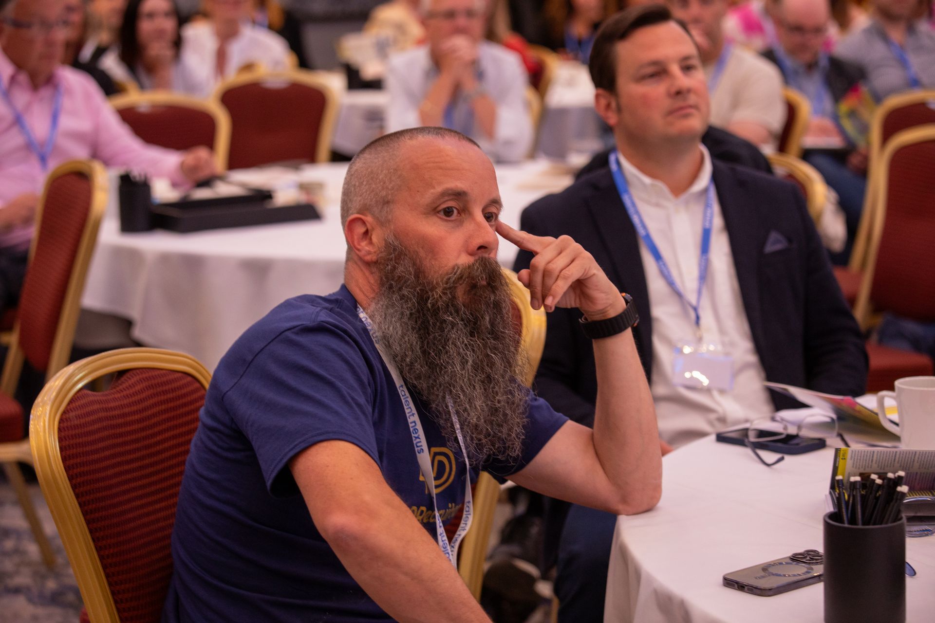 A man with a beard is sitting at a table in a conference room.