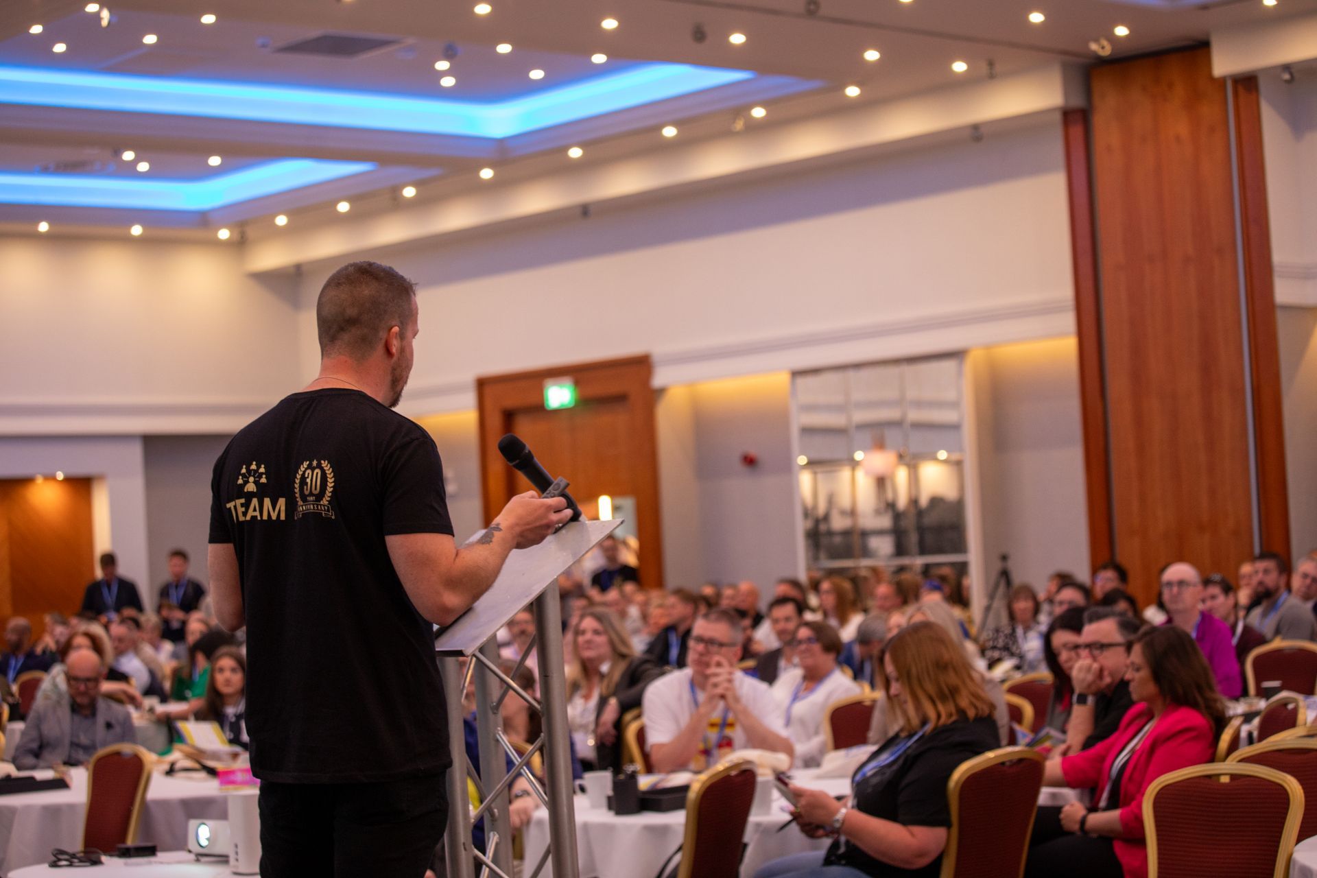 A man is standing at a podium giving a presentation to a large group of people.