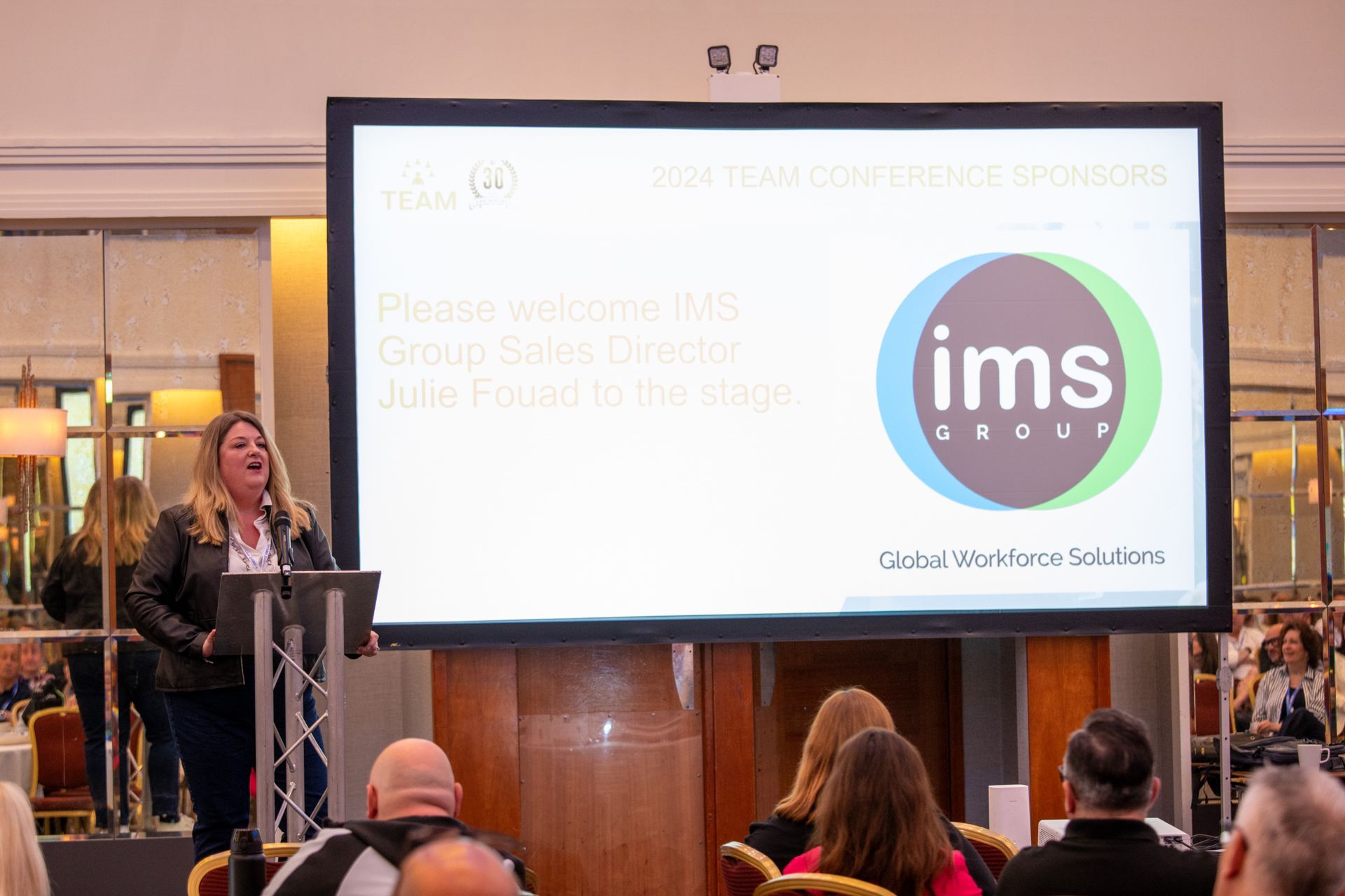 A woman is giving a presentation in front of a large screen.