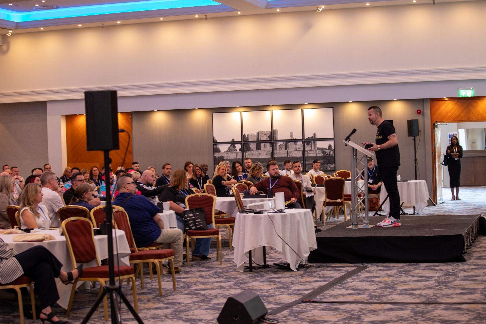 A man is standing on a stage giving a presentation to a large group of people.