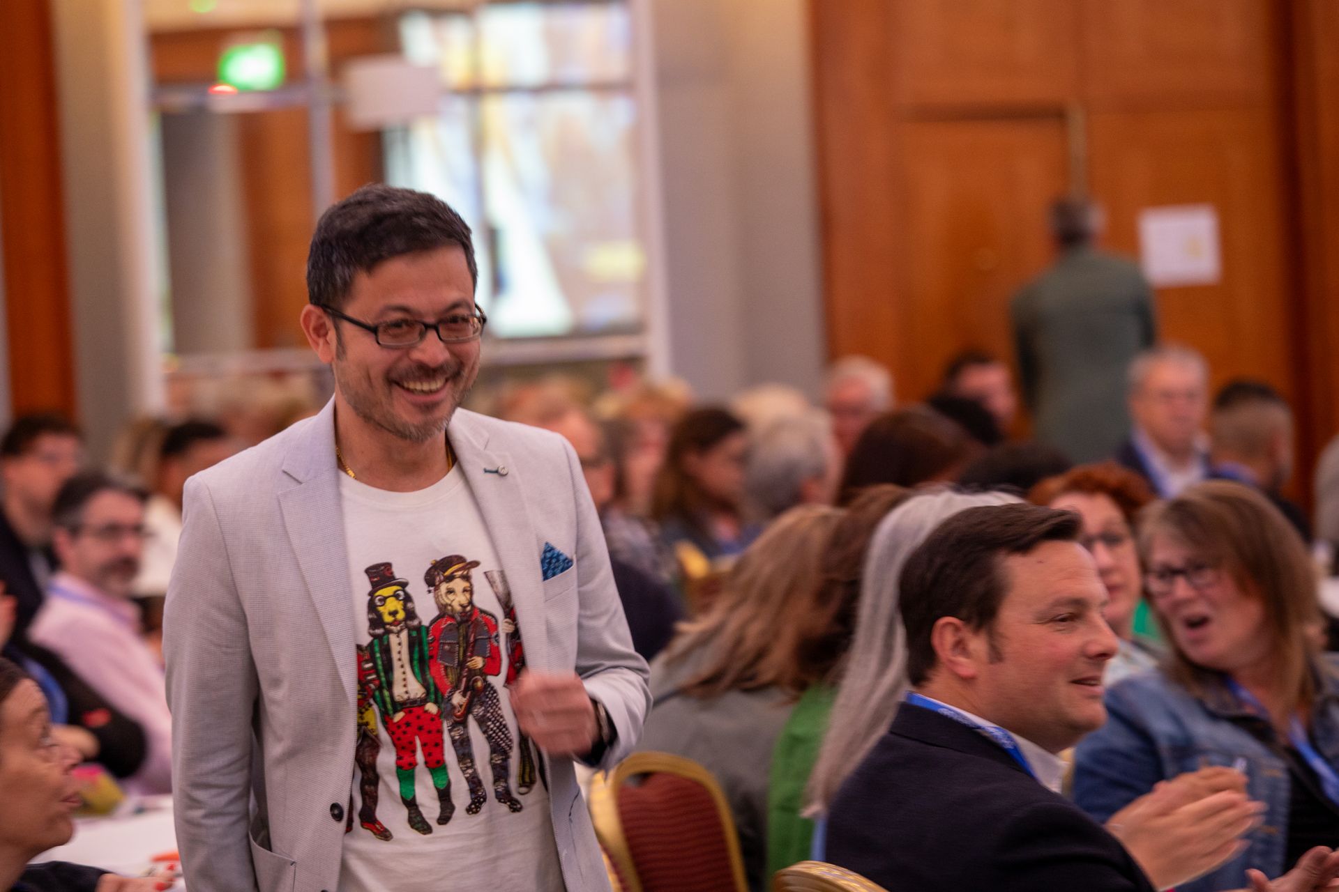 A man in a suit and a t-shirt is walking through a crowd of people at a conference.