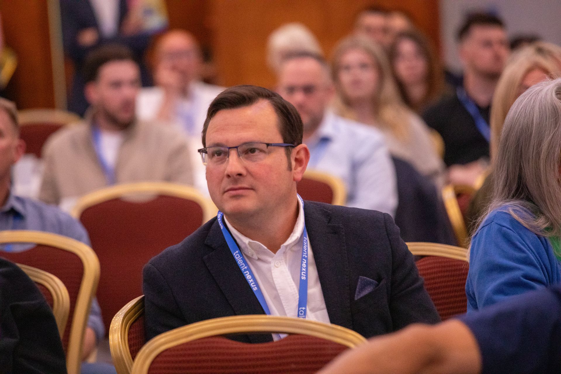 A man in a suit and tie is sitting in a row of chairs at a conference.