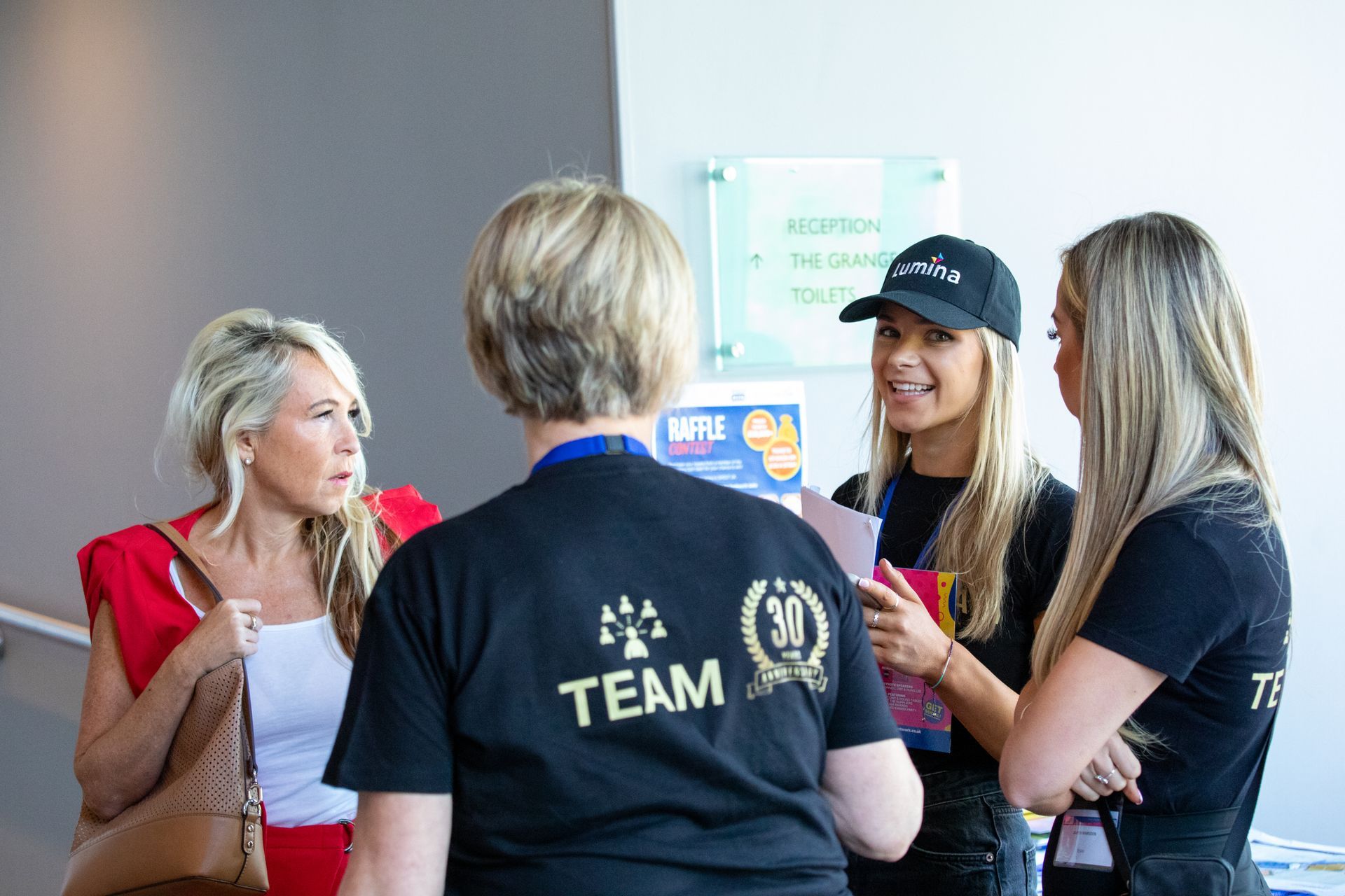 A group of women are standing in a room talking to each other.