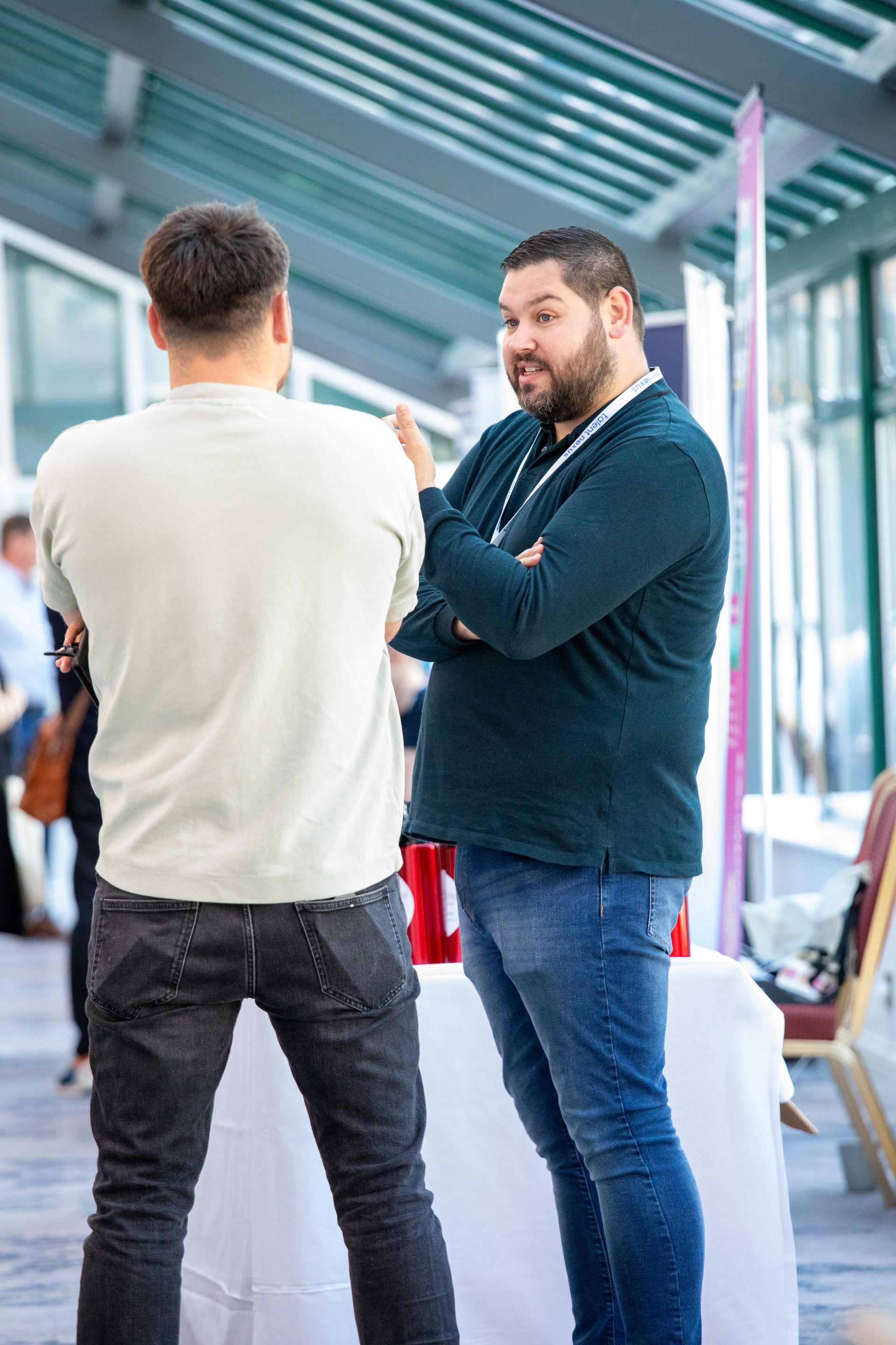 Two men are standing next to each other and talking in a room.