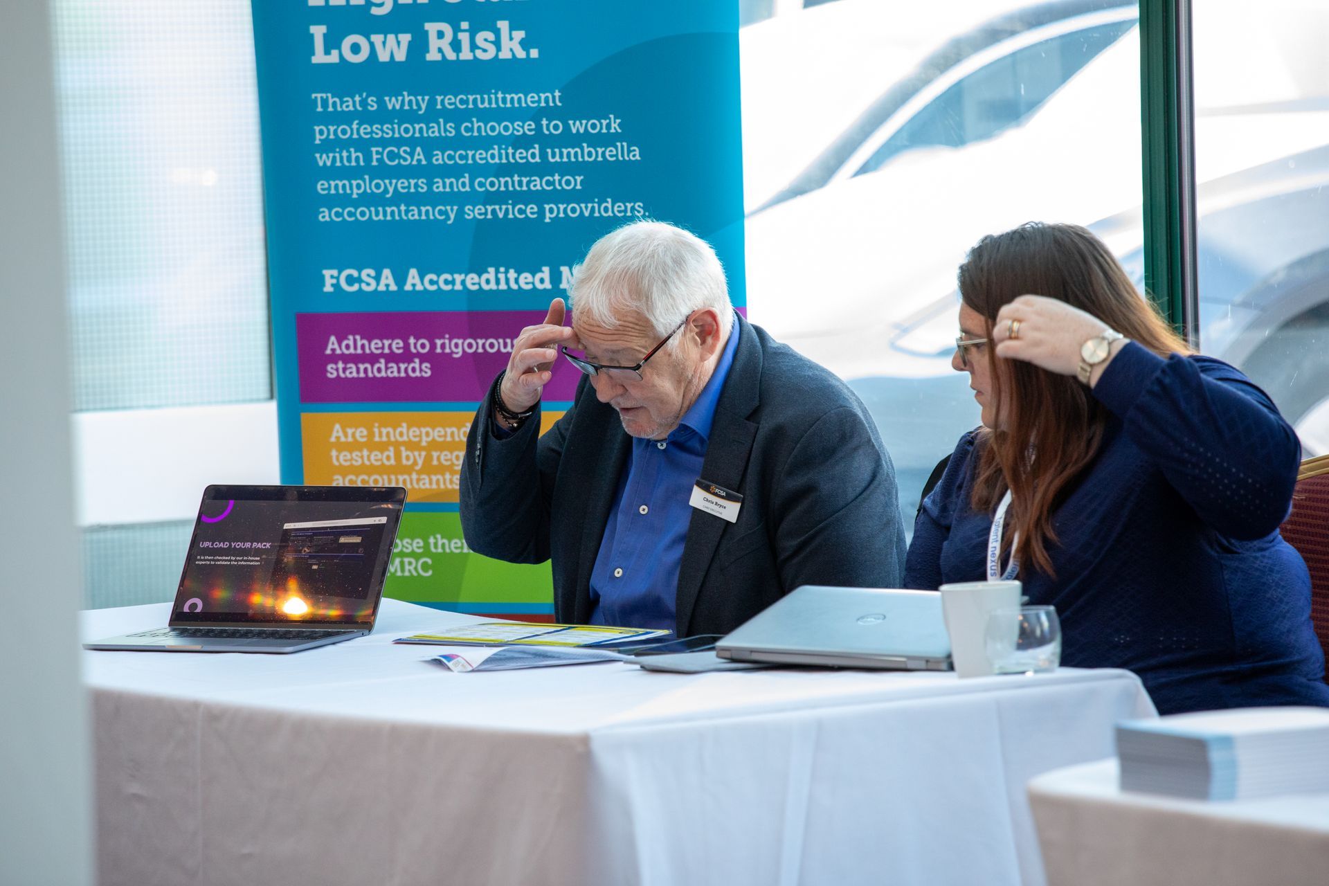 A man and a woman are sitting at a table looking at a laptop.